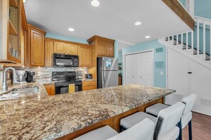 A kitchen with granite countertops, wooden cabinets, stainless steel appliances, and a bar area with stools. - On the Intracoastal | Pool | Fishing Pier | Walk to Beach | Indian Sands B3 (Indian Shores)