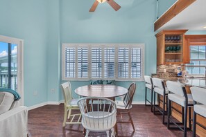 A dining area with a round table and chairs, a kitchen with bar stools, and a view through large windows. - On the Intracoastal | Pool | Fishing Pier | Walk to Beach | Indian Sands B3 (Indian Shores)