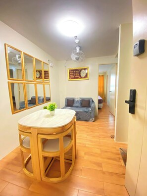 A room with a wooden dining table, a sofa, a wall clock, and a ceiling fan.