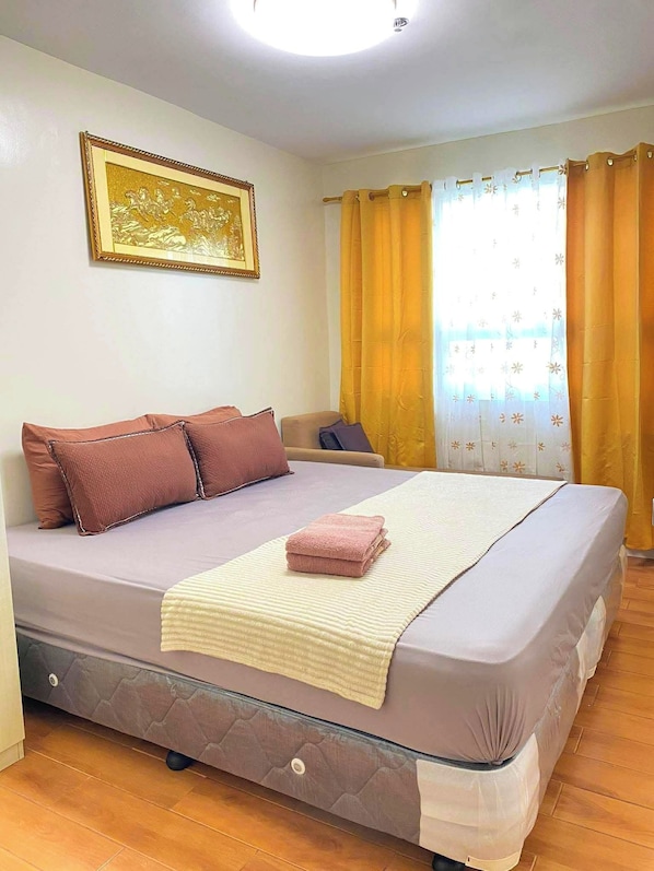 A bedroom with a bed, pillows, a blanket, a headboard, a window with curtains, and a wall-mounted picture.