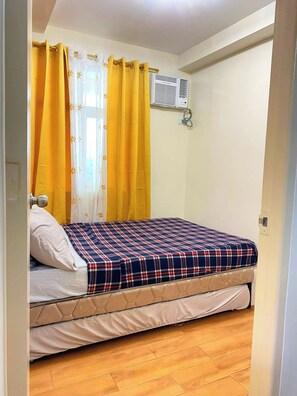 Ein Schlafzimmer mit einem Bett, gelben Vorhängen, einer Klimaanlage und Holzböden.