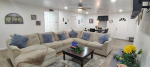 A living room with a sectional sofa, a coffee table, and a dining area with a table and chairs. - Brand New Remodel Off I-30 Mins to Buc-ee's w/ Ample Parking (Benton)