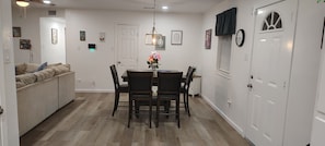 A dining area with a table and chairs, a sofa, a door, and a clock on the wall. - Brand New Remodel Off I-30 Mins to Buc-ee's w/ Ample Parking (Benton)
