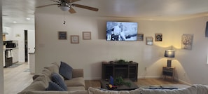 Un salon comprenant une télévision, un ventilateur de plafond, un canapé, une table basse et une table d’appoint avec une lampe.