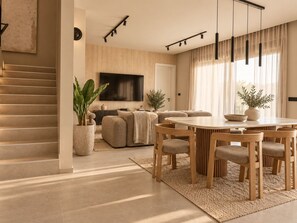 A modern living room with a dining area, a staircase, and a large TV. - Villa Amoa - Luxury 4-Bedroom Beachfront Villa (Lopar)