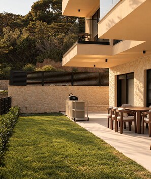 Eine moderne Terrassengruppe mit Esstisch, Grill und einer Wand aus Naturstein.