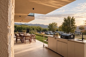 Eine Außenpatio mit Essbereich, Grillstation und Blick auf einen Parkplatz und Berge.