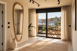 Un intérieur moderne agrémenté d’un grand miroir, d’un coin repas offrant une vue sur la mer et d’une porte-fenêtre coulissante donnant sur une terrasse extérieure.