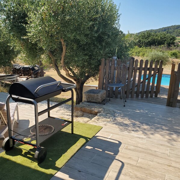 A barbecue grill on a patio with a pool and wooden fence in the background.