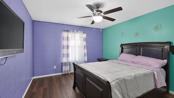 A bedroom with a bed, a ceiling fan, a window with curtains, and a wall-mounted TV.