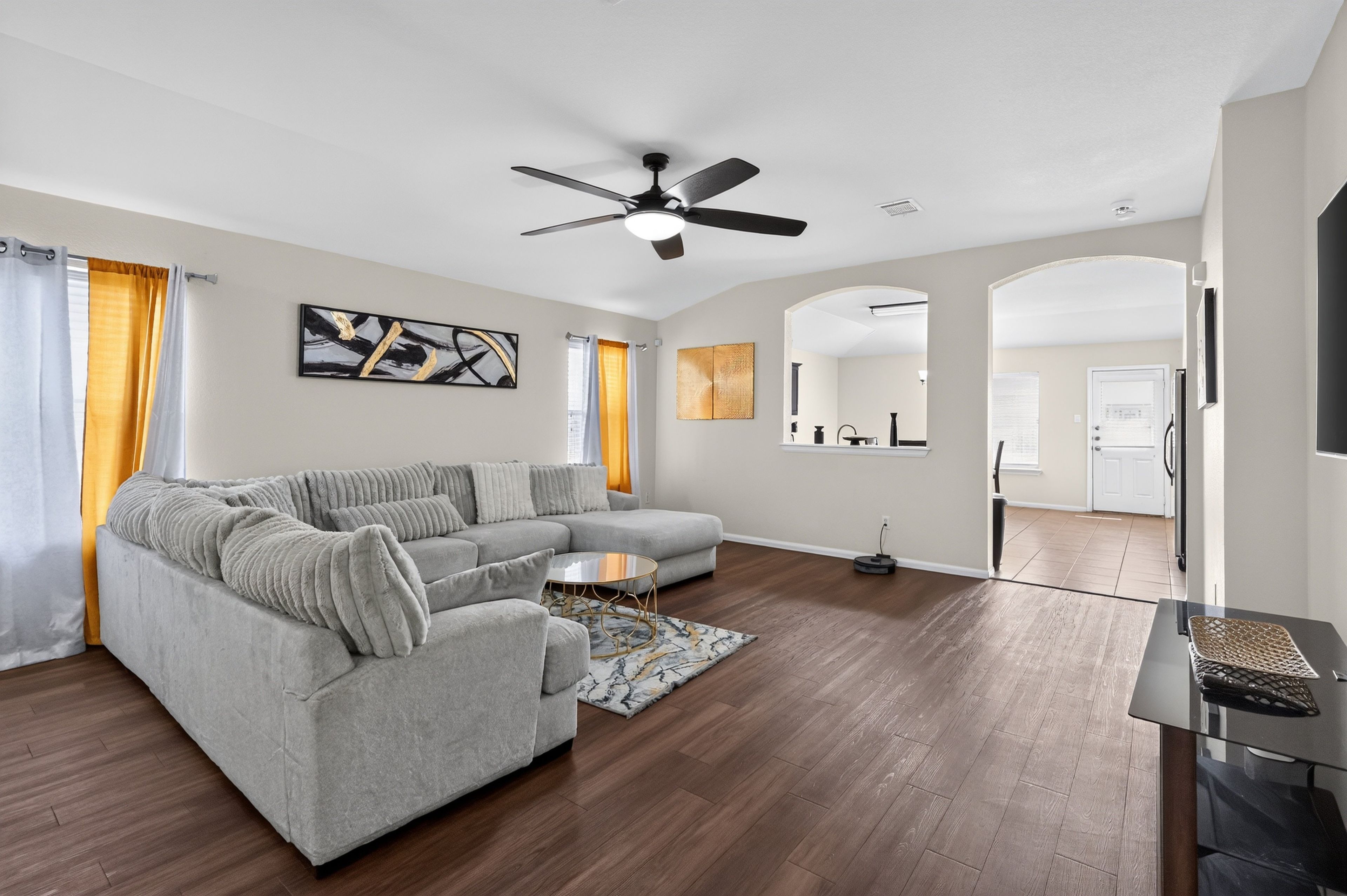 Un salon moderne avec un canapé d’angle, une table basse et un ventilateur de plafond.