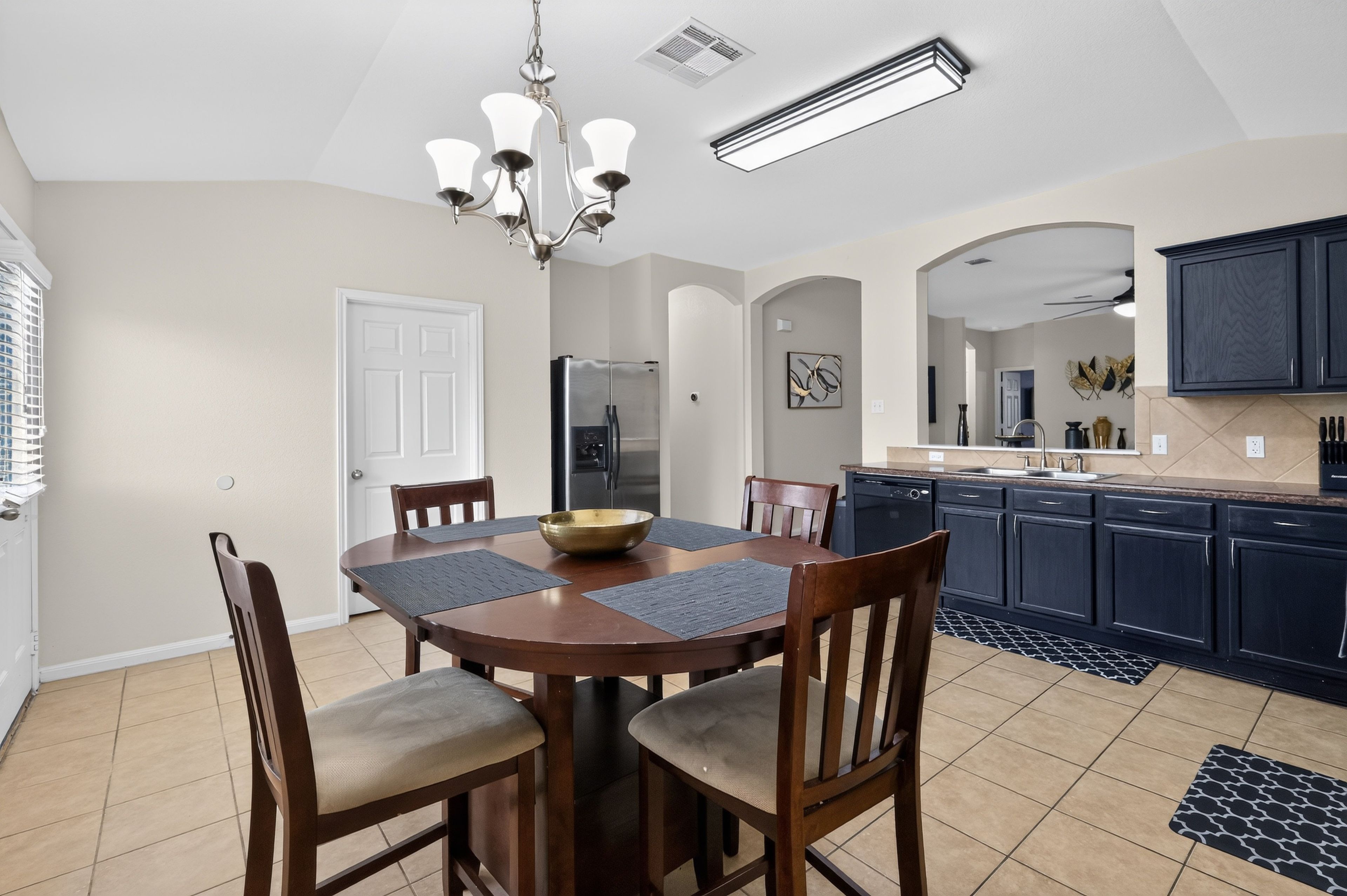 A modern kitchen with a dining area, featuring a round table with chairs, a built-in oven, and a refrigerator.
