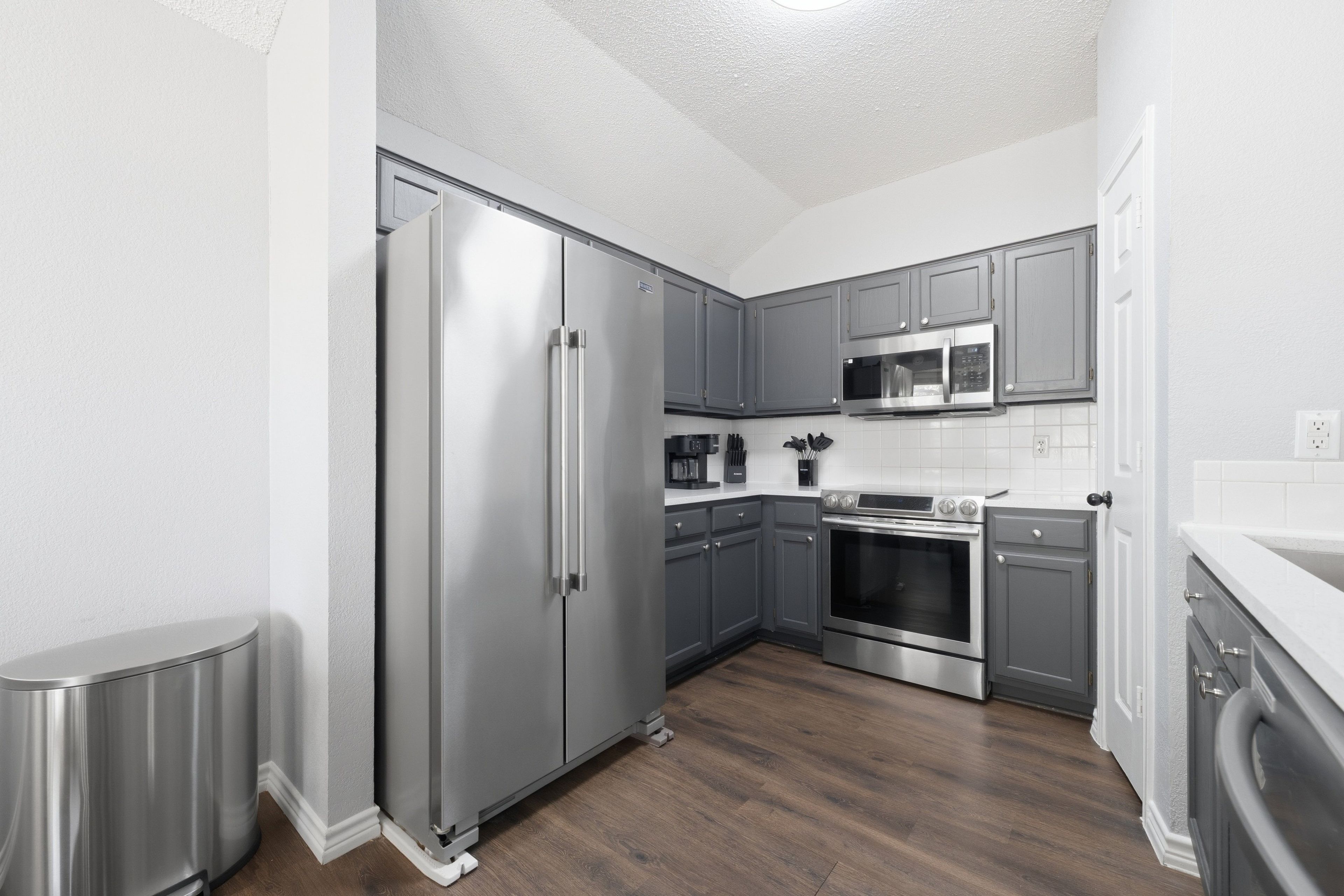 A modern kitchen with stainless steel appliances, grey cabinetry, and a wooden floor.