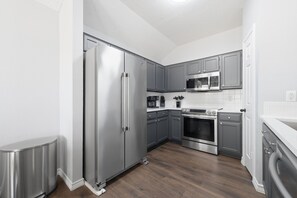 A modern kitchen with stainless steel appliances, grey cabinetry, and a wooden floor. - New! Cozy 3BR Retreat Near Fort Hood Killeen (Killeen)