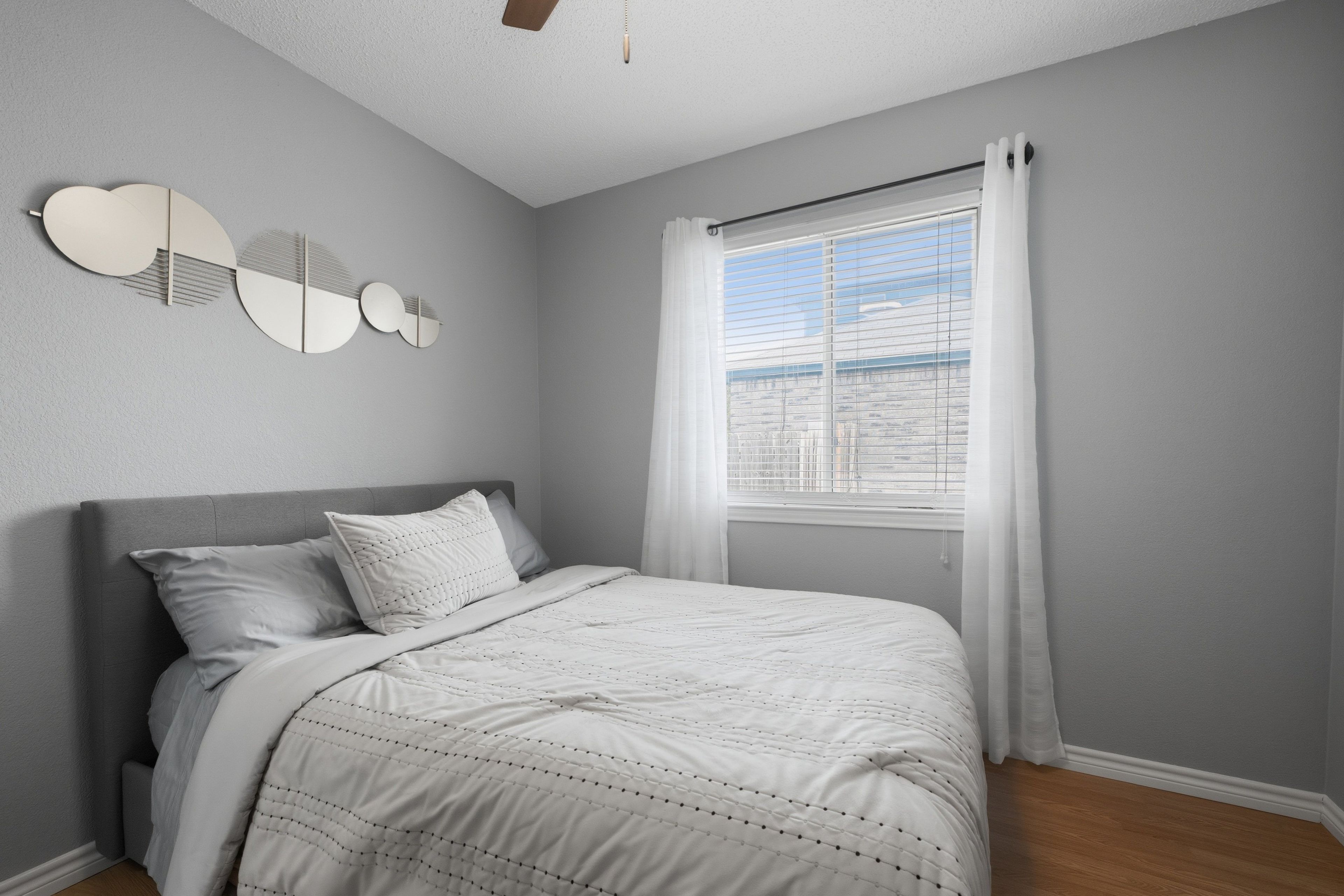 Une chambre à coucher avec un lit, une fenêtre avec des rideaux et un luminaire fixé au mur.