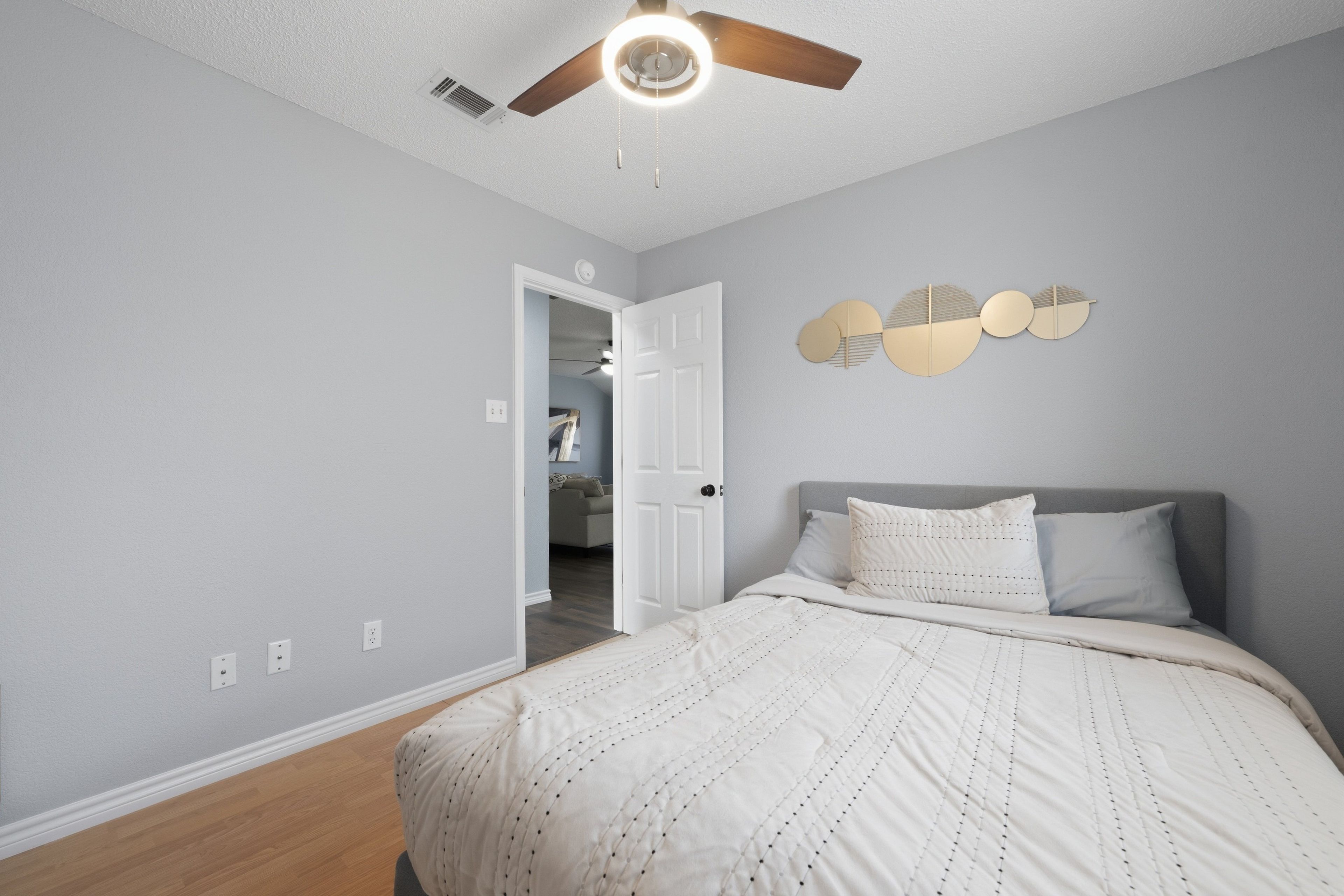 Un dormitorio con cama, ventilador de techo, una puerta que da a otra habitación y un adorno en la pared.