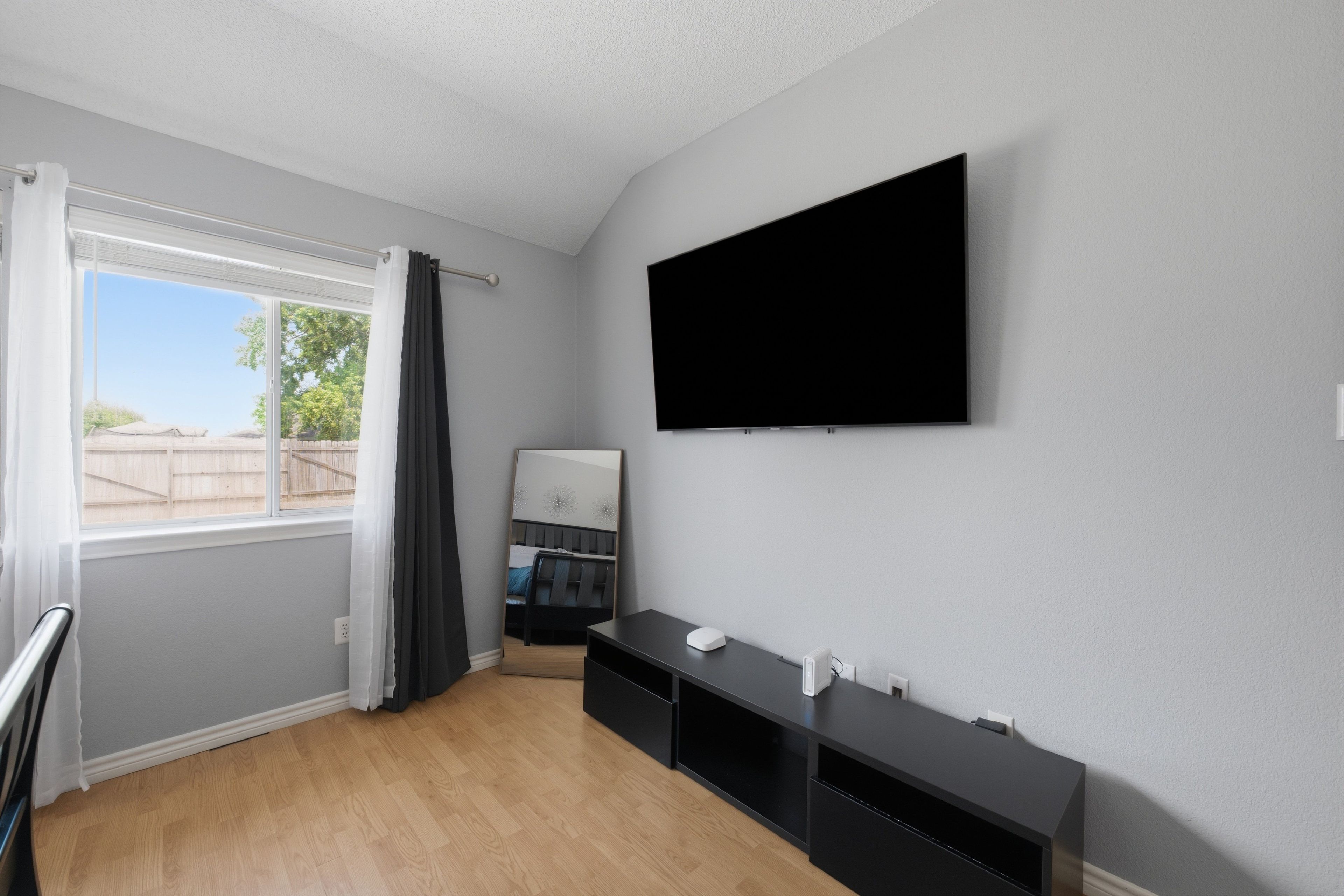 A modern room with a large window, a flat-screen TV mounted on the wall, and a dark wooden floor.