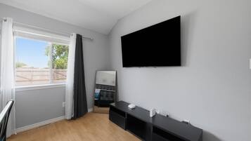 A modern room with a large window, a flat-screen TV mounted on the wall, and a dark wooden floor.