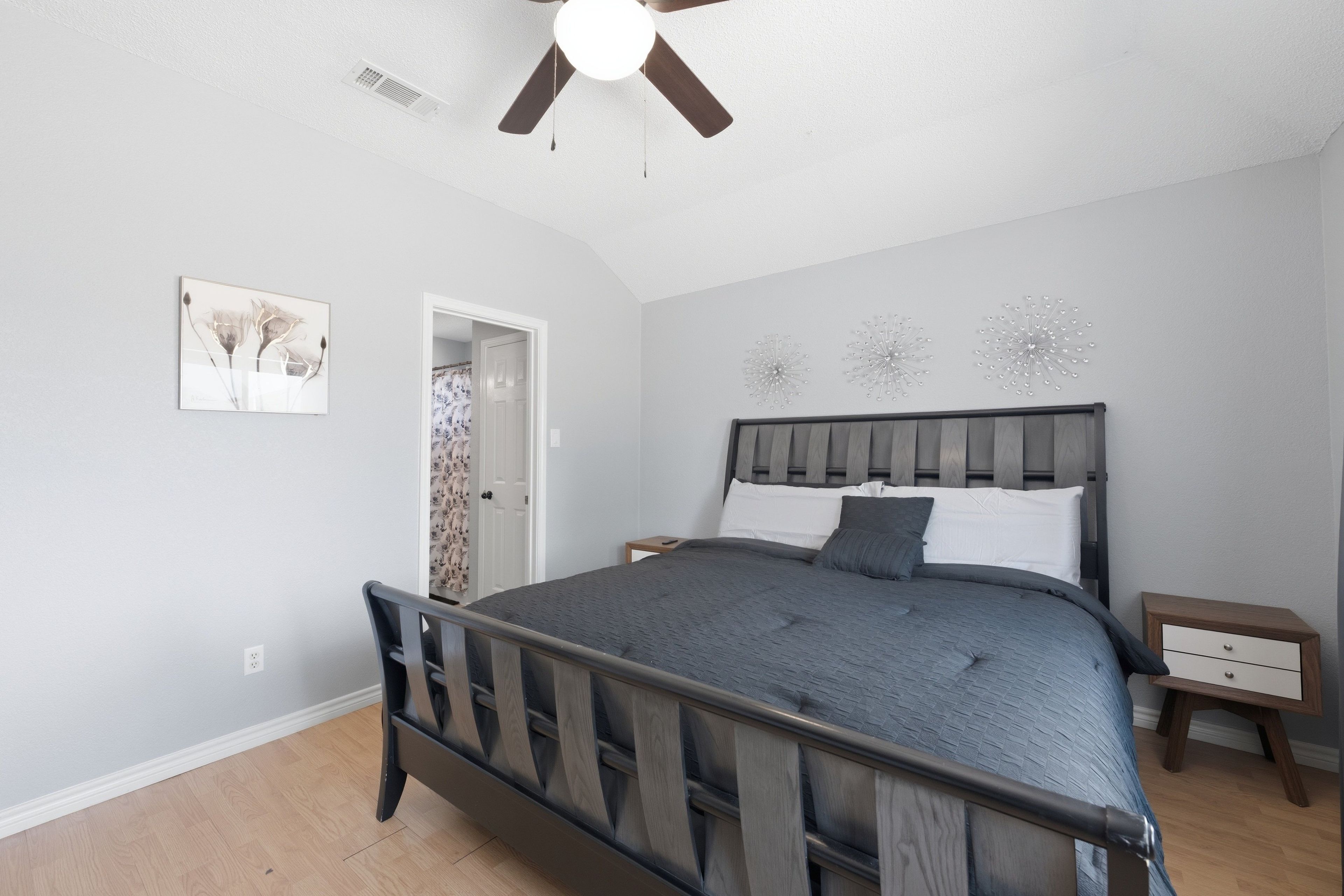 A bedroom with a bed, a ceiling fan, a door, and a nightstand.