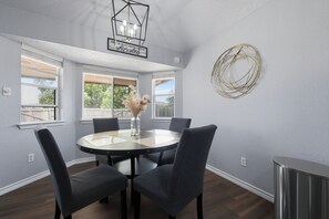 A dining area with a round table, four chairs, a vase with dried flowers, a wall-mounted light fixture, and a decorative circular piece. - New! Cozy 3BR Retreat Near Fort Hood Killeen (Killeen)