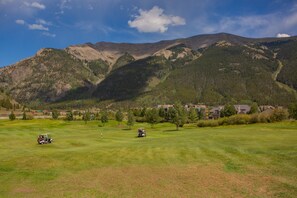 Ein Golfplatz mit Bergkulisse, ein Golfwagen und ein klarer Himmel.