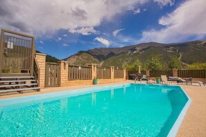A swimming pool with a mountain backdrop, surrounded by a fenced area with lounge chairs and a stone wall. - Cv105 Copper Valley 1 Bedroom Condo (Copper Mountain)