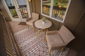 Ein überdachter Patio-Bereich mit Korbmöbeln, einem runden Tisch und einem Blumentopf sowie einem gemusterten Boden.
