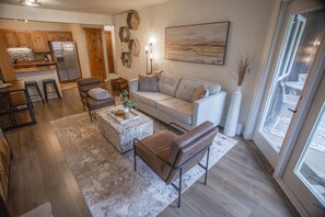 A modern living room with a sofa, coffee table, and chairs. There is a kitchen in the background with a refrigerator and cabinets. - Cv105 Copper Valley 1 Bedroom Condo (Copper Mountain)
