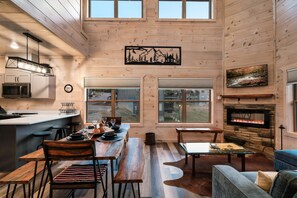 Amplia sala de estar con chimenea, pisos de madera y una mesa de comedor preparada para cuatro.