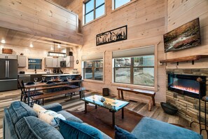 A spacious living area with a fireplace, a dining table, and a kitchen in the background. - Smokiedoki Lodge 3 Bedroom Cabin (Pigeon Forge)