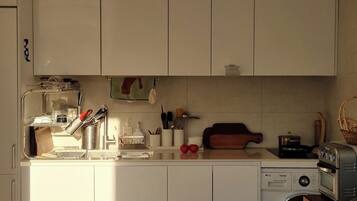 A compact kitchen with white cabinets, a washing machine, and a toaster.