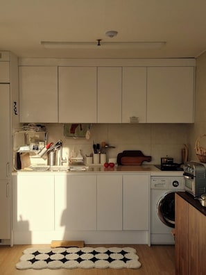 Ett kompakt kök med vita skåp, en tvättmaskin, en brödrost och en skärbräda i trä.