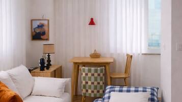 A room with a sofa, a bed, a table with a chair, and a window with curtains.