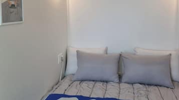 A bedroom with a bed, two pillows, a wall-mounted light, and a framed picture.