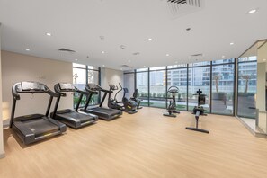 Ein modernes Fitnessstudio mit Laufbändern, Crosstrainern und einem Ergometer, ausgestattet mit großen Fenstern und Blick auf die Stadtlandschaft.