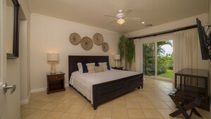Un dormitorio con una cama grande, un ventilador de techo, un televisor y una puerta corrediza de vidrio al exterior.