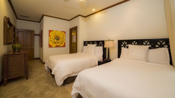 Habitación de hotel con dos camas, un ventilador de techo, un cuadro de una flor, un armario de madera y un espejo.