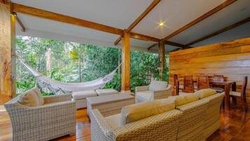 A room with wicker furniture, a hammock, and a view of lush greenery.
