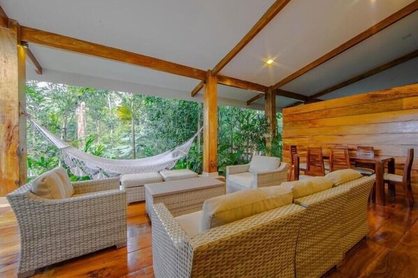 Une pièce meublée de mobilier en osier, avec un hamac et une vue sur une végétation luxuriante.