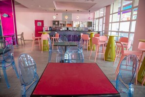 A modern cafe with a red table in the foreground, colorful chairs, and a bar area in the background. - Be-city Hotel Eilat (Eilat)
