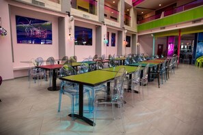 A spacious indoor area with multiple tables and chairs, a high ceiling, and artwork on the walls. - Be-city Hotel Eilat (Eilat)