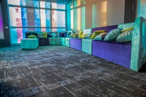 Un área de descanso moderna con un sofá modular, otomanas, ventanas amplias y una alfombra estampada.