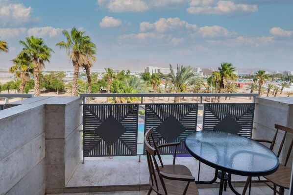 A balcony with a glass table and chairs, overlooking palm trees and a cityscape. - Be-city Hotel Eilat (Eilat)