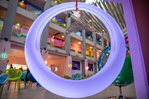Una lámpara circular con un elemento colgante, ubicada en un espacio interior de varios niveles con zonas de estar y una escalera.