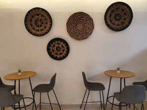 A room with a wall-mounted decorative plate, two round tables with chairs, and a small potted plant on each table. - Sea Princess Motel (Eilat)