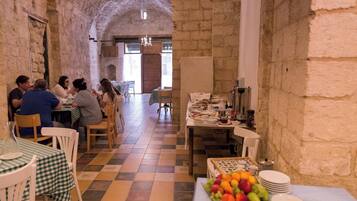 A restaurant with stone walls and a checkered floor, tables with green and white checkered tablecloths, and a fruit display.