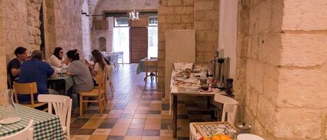 Un restaurante con paredes de piedra y suelo a cuadros, mesas con manteles de cuadros verdes y blancos, y una exhibición de frutas.