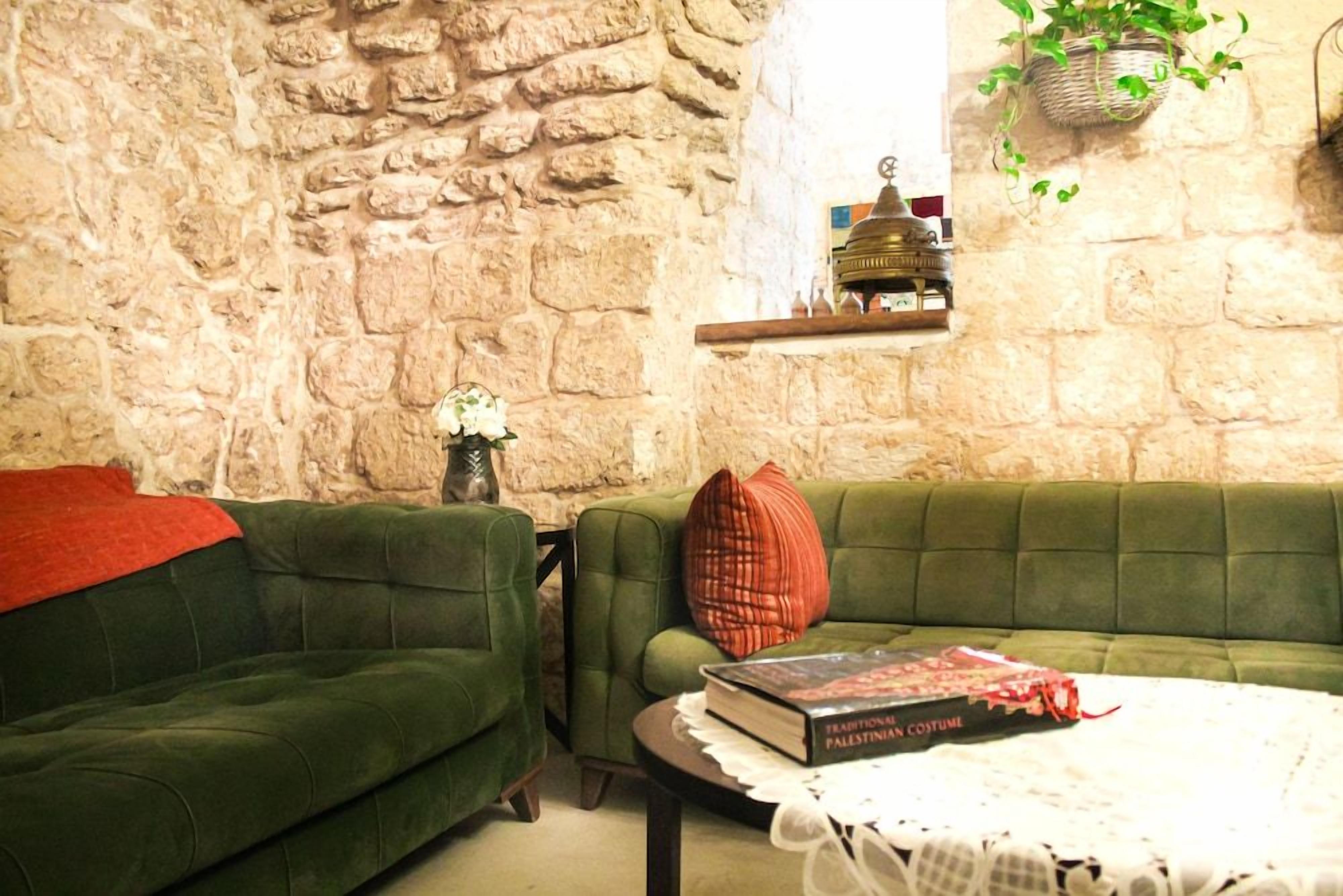 A room with a stone wall, two green sofas, a small table with a book, and a hanging plant.