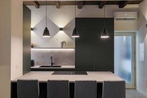 Eine moderne Küche mit Kochinsel, Pendelleuchten und einem eingebauten Kühlschrank.