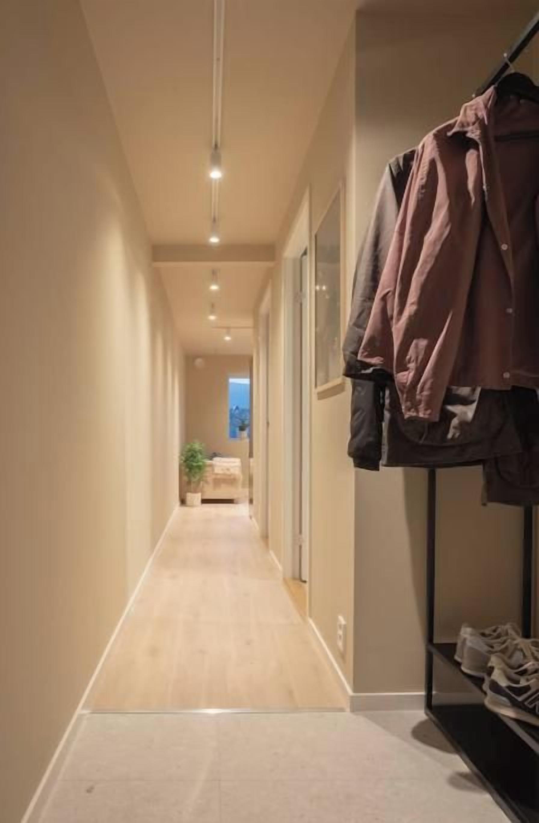 A hallway with a wooden floor, a coat rack with jackets, and a shoe rack.